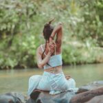 Mujer practicando yoga al aire libre junto al agua en la naturaleza