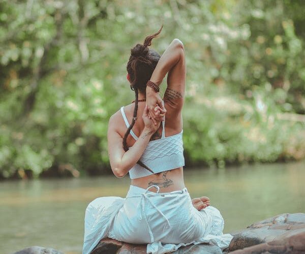 Mujer practicando yoga al aire libre junto al agua en la naturaleza