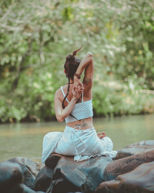 Mujer practicando yoga al aire libre junto al agua en la naturaleza